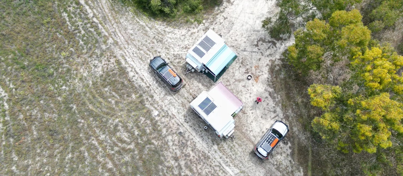 Due camper in una piazzola sabbiosa circondata dalla vegetazione australiana