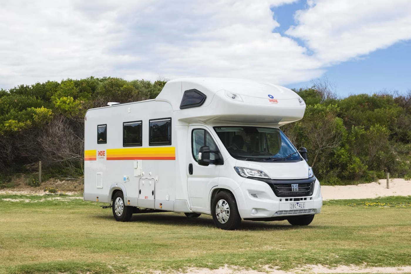 Camper a noleggio Indie Campers parcheggiato vicino alla vegetazione costiera in Australia